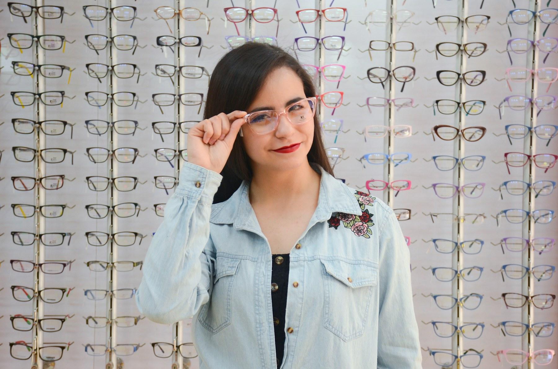 A woman trying on glasses in front of a wall of frames